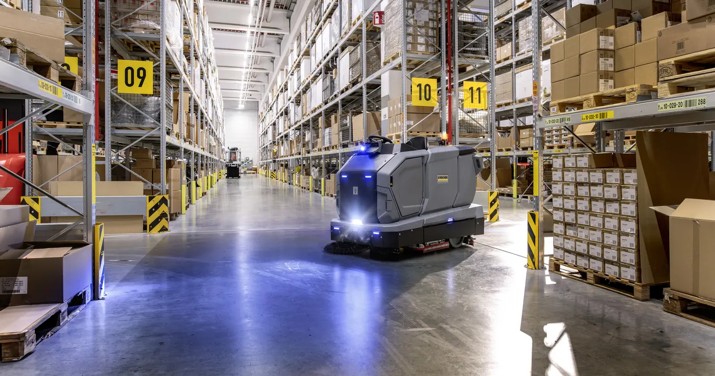 Kärcher KIRA B 200 : Bandeau large : robot KIRA B 200 dans une allée d'entrepôt, éclairage bleu au sol (1600×841)